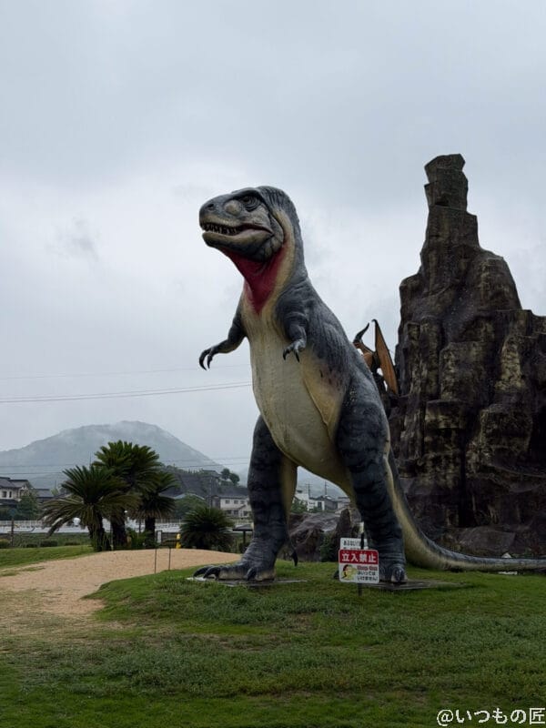 iPhone 17 Pro カメラ 曇り空の下に立つティラノサウルスのオブジェ